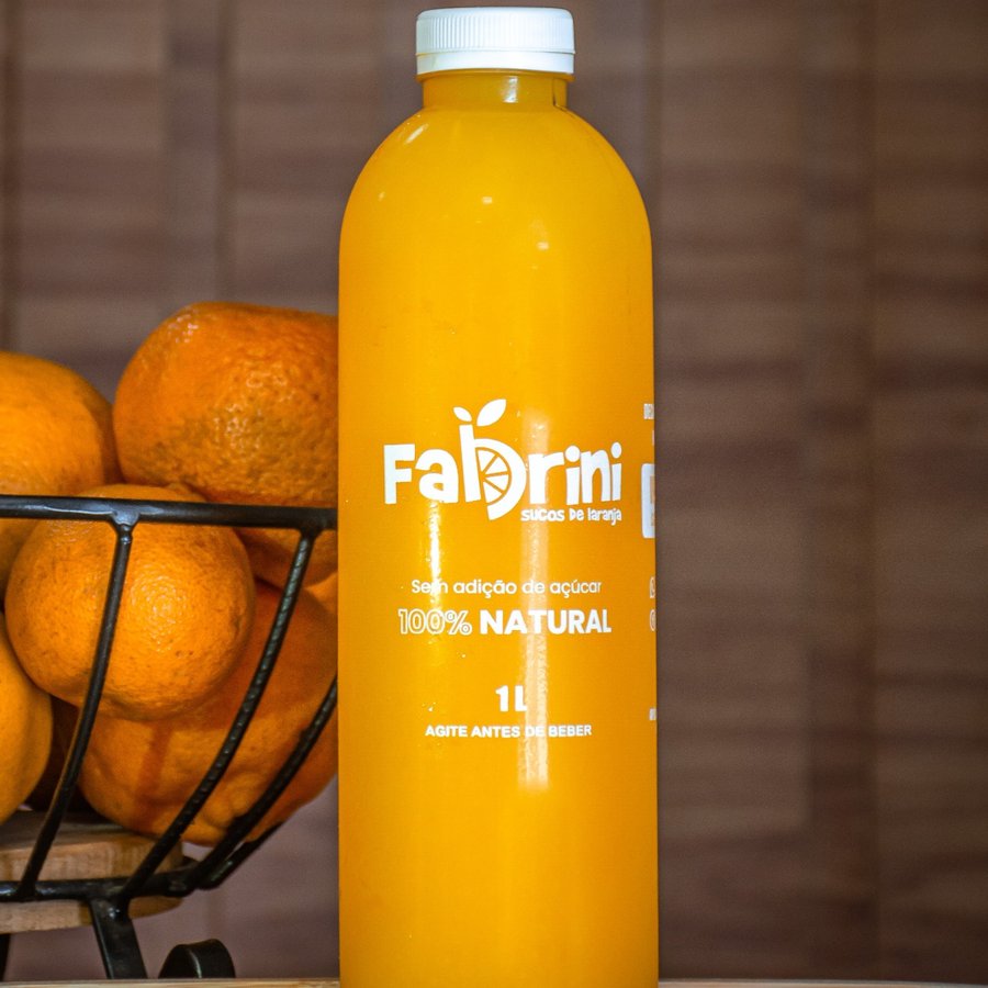Garrafa de suco de laranja Fabrini de 1 litro ao lado de uma cesta de laranjas